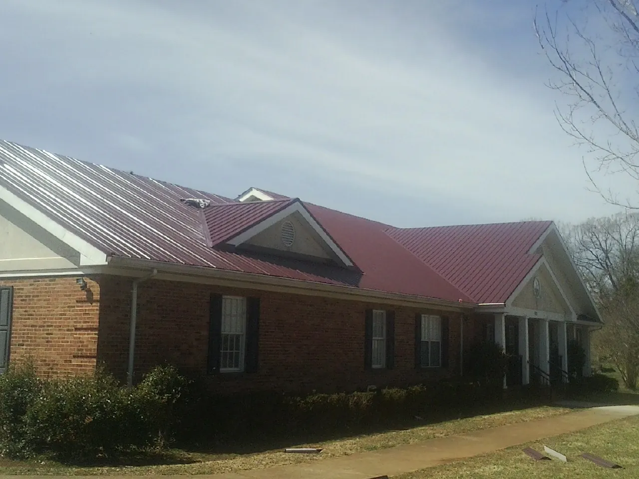 Red metal roof with gabled entries on a long brick building, from a Hail Damage Roof Repair job in Port Carbon