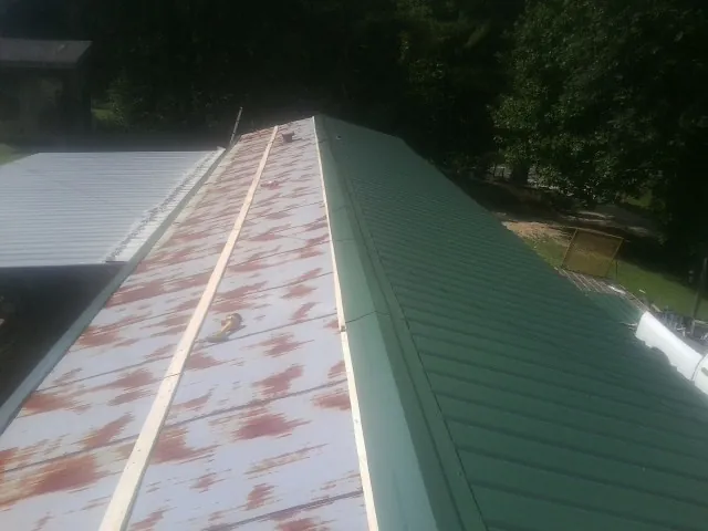 Old rusted panels beside newly installed green metal roofing — Wind Damage Roof Repair by Roofing Brothers in Port Carbon