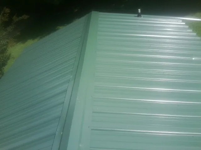 New green metal panels meeting at the ridge of a roof — Flat Roof Repair work by our crew in Port Carbon
