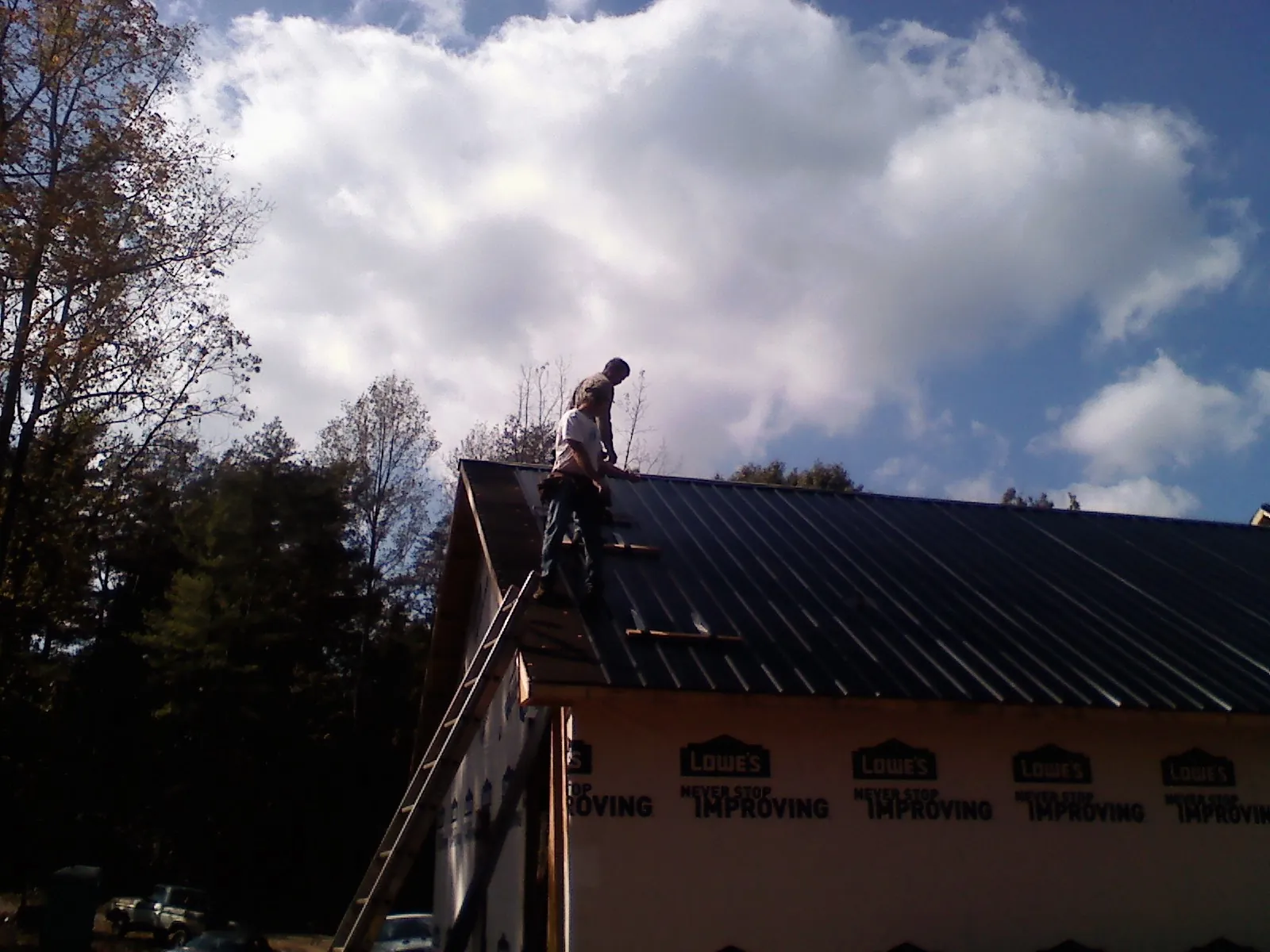 Roofer fastening dark metal panels high against a cloudy sky, from a Roof Inspection job in Port Carbon