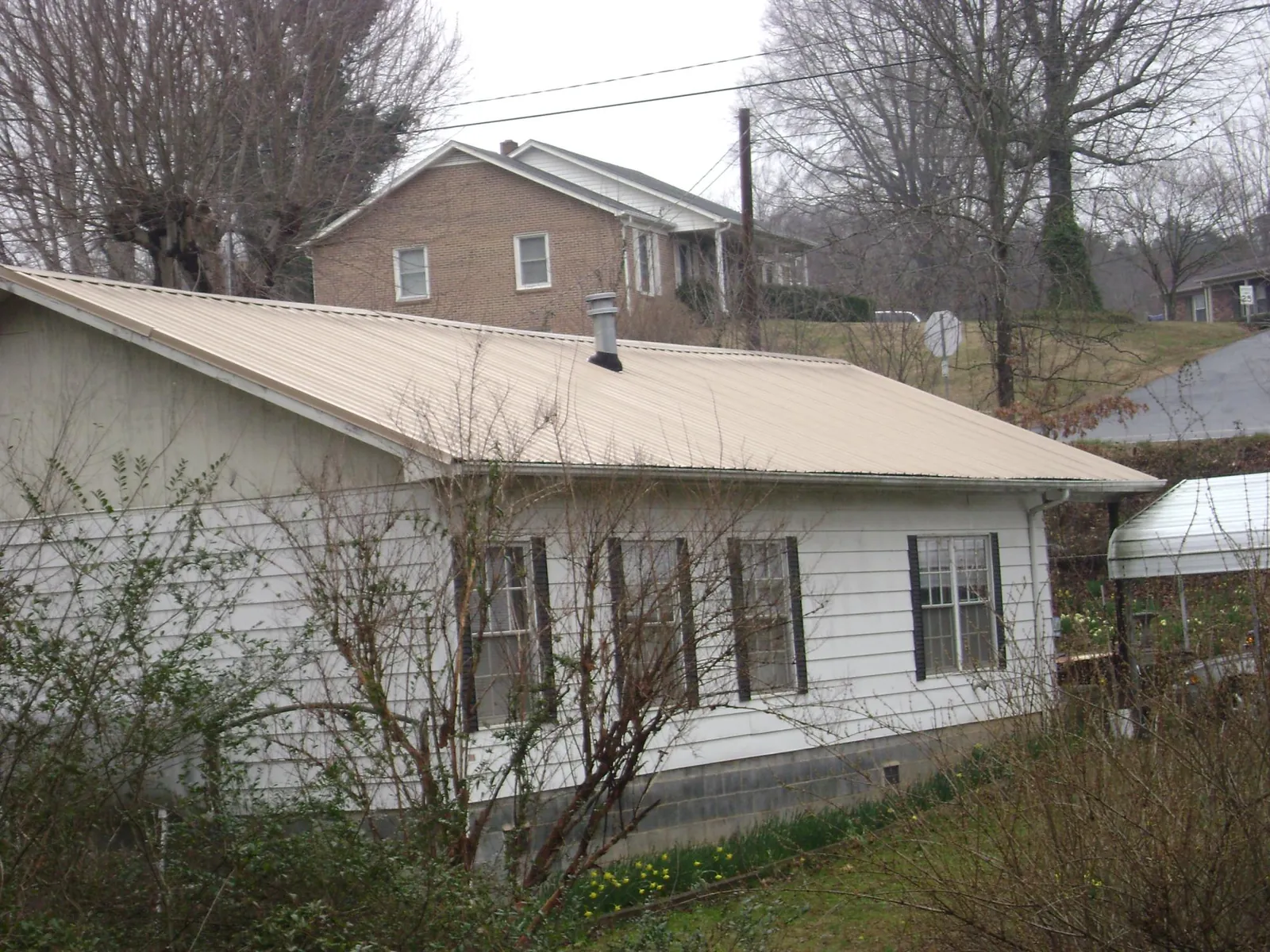 Tan metal roof on a white sided house set into a hillside — Commercial Roofing by Roofing Brothers in Port Carbon